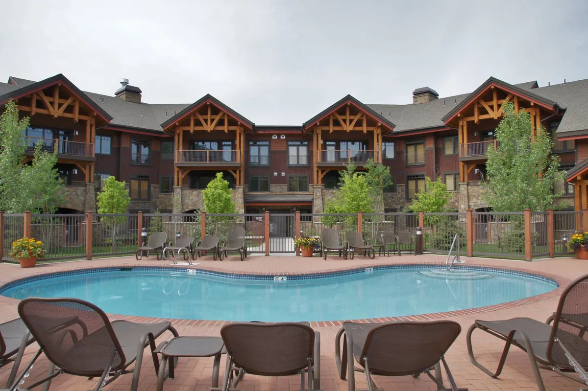 A bright swimming pool is surrounded by lounge chairs and the residential building, with children and adults playing in the water and sunbathing. The landscaping and inviting setting suggest a lively, family-oriented atmosphere for relaxation and fun.