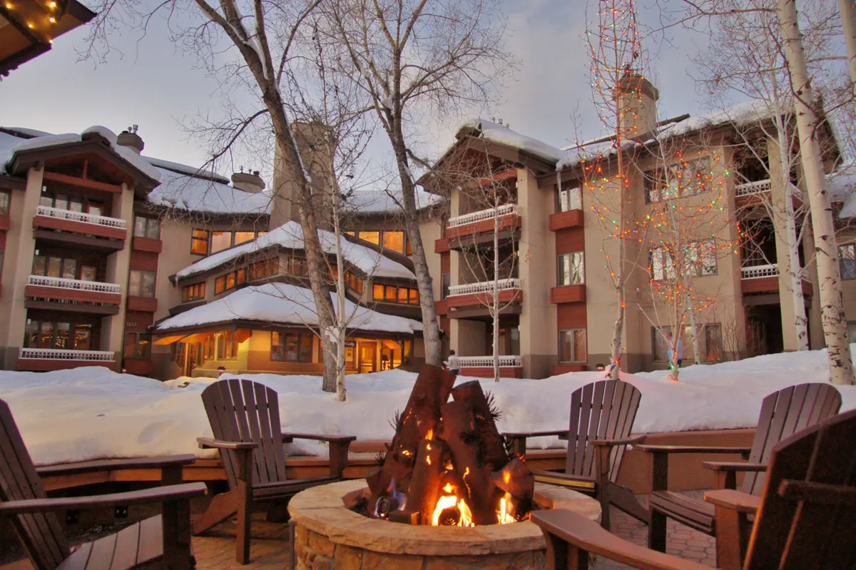An inviting fire pit set in a snow-covered landscape, with decorated trees and the building's facade in view. It evokes a sense of warmth and camaraderie, with space for social gatherings or quiet evenings under the stars during wintertime.