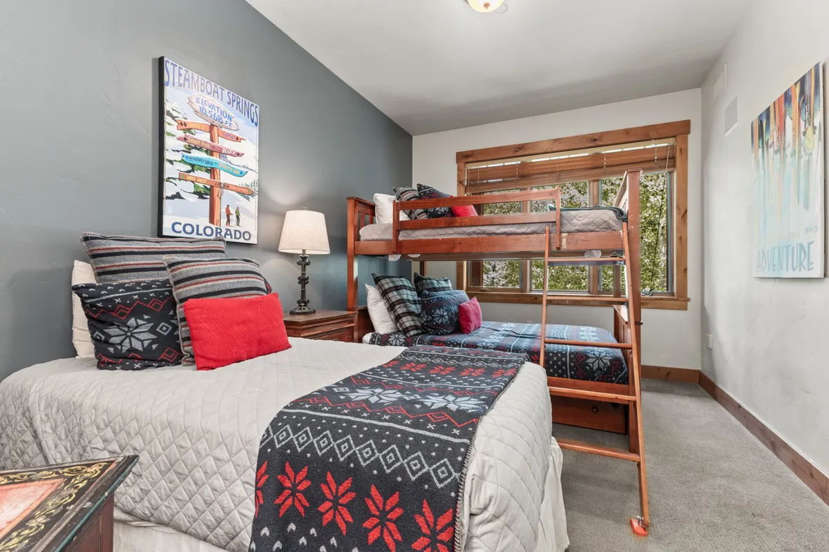 A cheerful, playful bedroom with double-over-double bunk beds and decorative throw blankets. The space is accented by lively wall artwork, making it especially appealing for children or singles. The playful setup is perfect for sleepovers or flexible family arrangements.