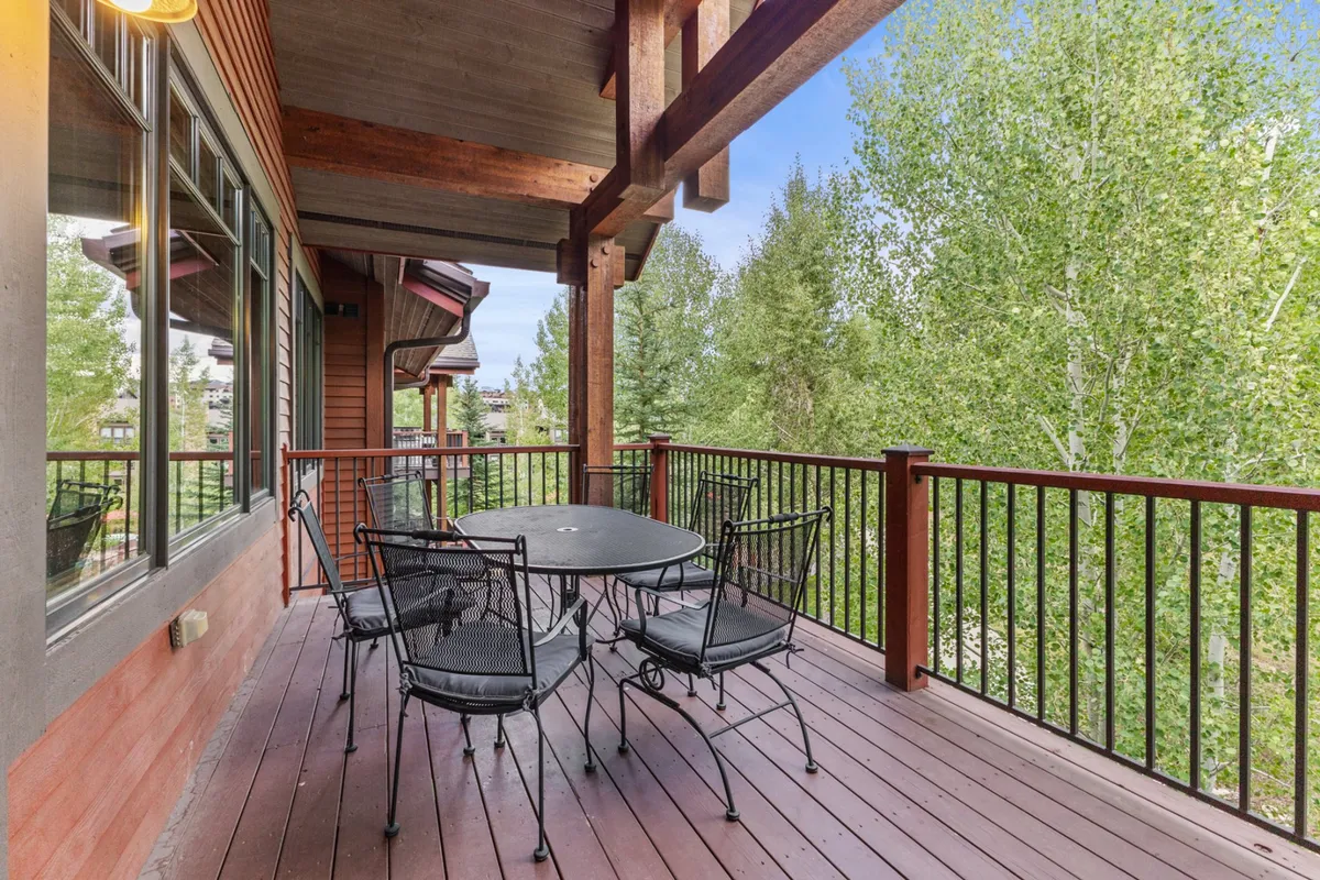 A tranquil covered deck with an outdoor dining table surrounded by trees and sturdy railings. The setting suggests opportunities for al fresco dining, sunset views, and enjoying the natural landscape, extending the communal indoor ambiance to the outdoors.