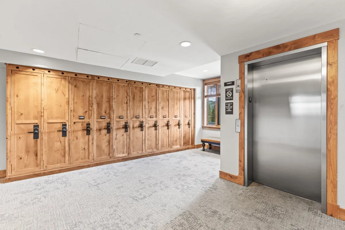 A functional lobby area featuring wooden lockers and an elevator, illuminated by natural light. Guests can store ski equipment or other outdoor gear here, highlighting the convenience for adventure seekers.
