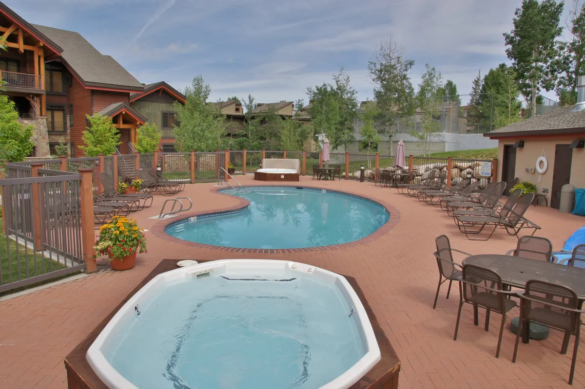 A spacious outdoor pool and hot tub area, bordered by lounge chairs and landscaped gardens. The scene exudes relaxation and invites guests to enjoy the outdoors, whether sunbathing, swimming, or socializing amidst mountain scenery.