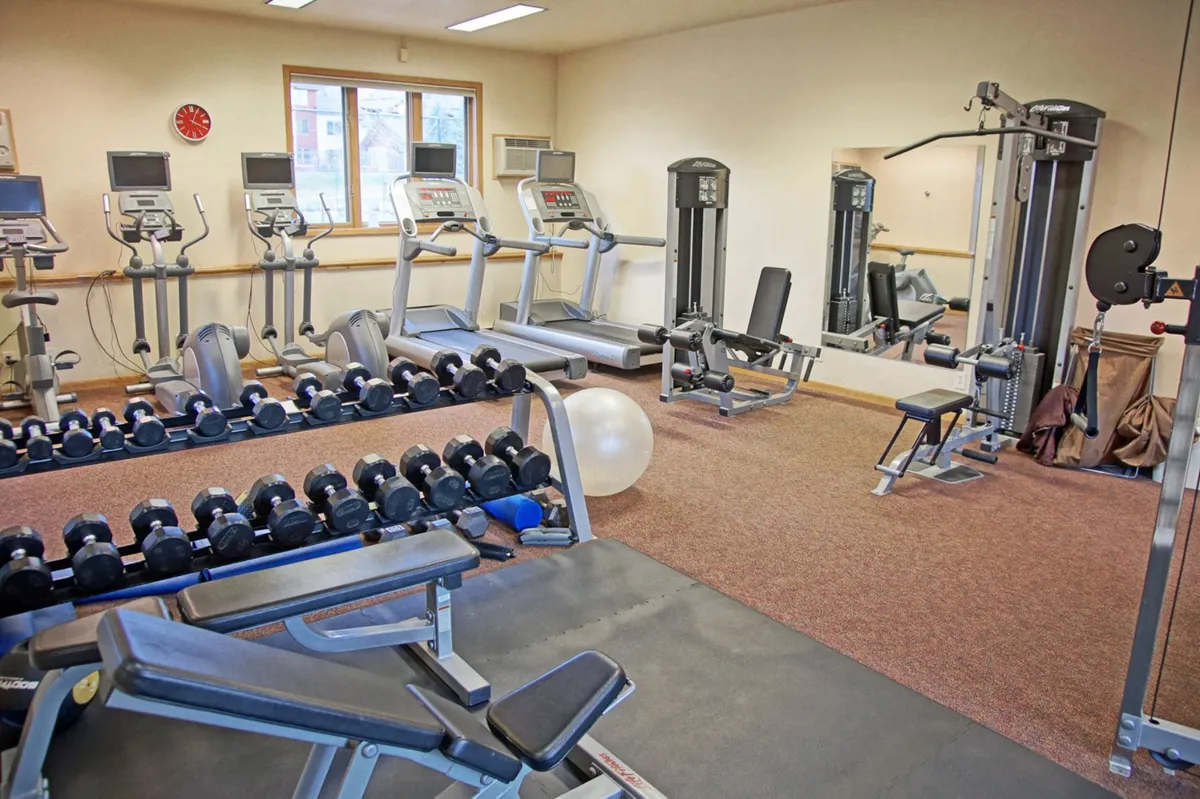 A bright, modern fitness center equipped with treadmills, dumbbells, weight machines, and an exercise ball. The energetic atmosphere supports both solo workouts and community fitness events.