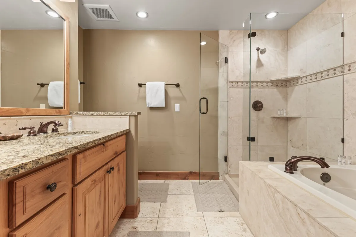 A spa-like bathroom with a granite countertop, glass shower enclosure, separate bathtub, wooden cabinetry, and a mirrored vanity. The space is tranquil and inviting, ideal for luxurious self-care routines.